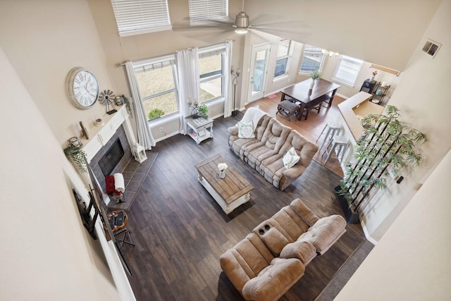 living room with a tile fireplace, a towering ceiling, dark wood-type flooring, and ceiling fan