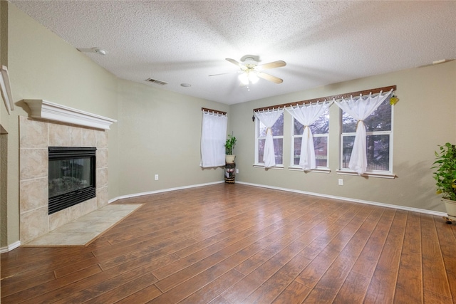 unfurnished living room featuring dark hardwood / wood-style flooring, a textured ceiling, a tile fireplace, and ceiling fan