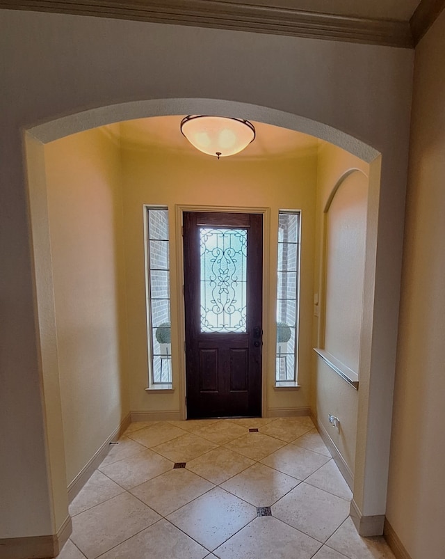 entrance foyer featuring arched walkways, light tile patterned floors, baseboards, and crown molding