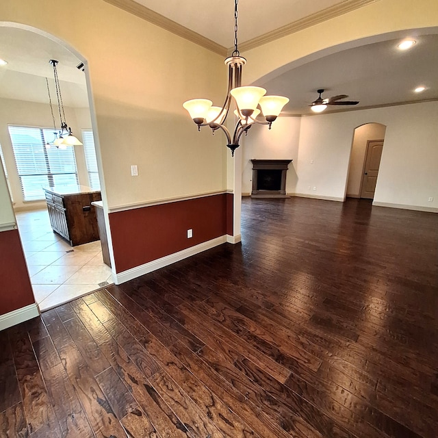 unfurnished living room with arched walkways, wood-type flooring, baseboards, and ceiling fan with notable chandelier