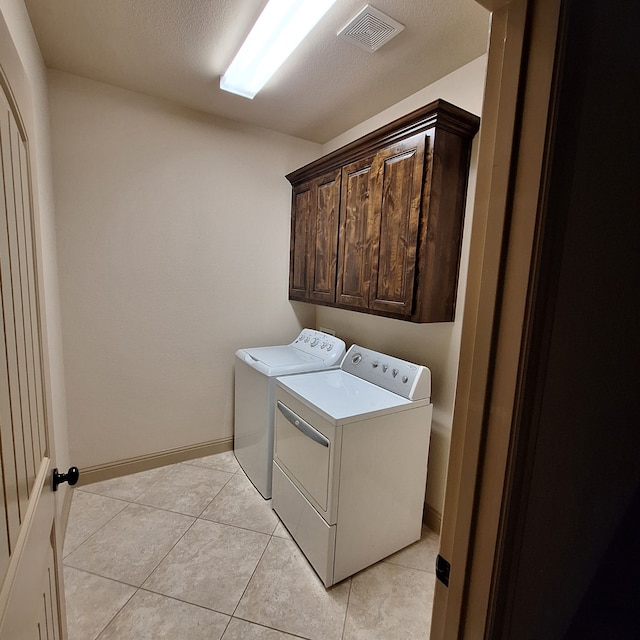 laundry area with light tile patterned floors, a textured ceiling, washing machine and dryer, visible vents, and cabinet space