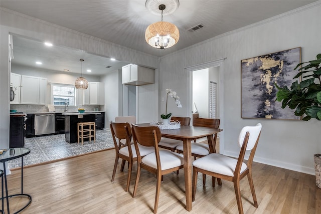 dining room with ornamental molding, a notable chandelier, and light hardwood / wood-style floors