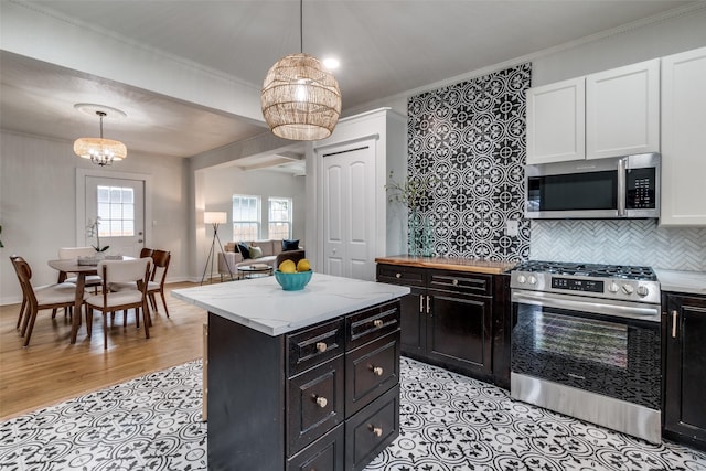 kitchen featuring ornamental molding, stainless steel appliances, hanging light fixtures, and white cabinets