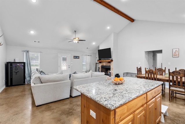 kitchen featuring a kitchen island, a stone fireplace, high vaulted ceiling, beamed ceiling, and ceiling fan