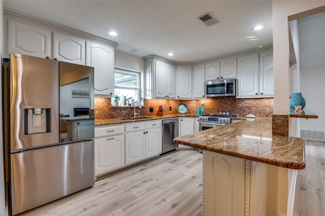 kitchen with stone counters, sink, white cabinets, kitchen peninsula, and stainless steel appliances