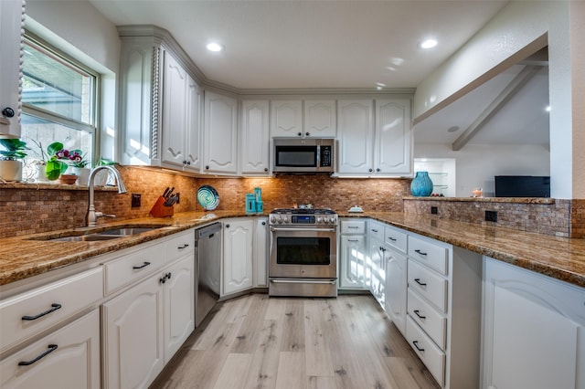 kitchen with white cabinetry, appliances with stainless steel finishes, sink, and dark stone counters