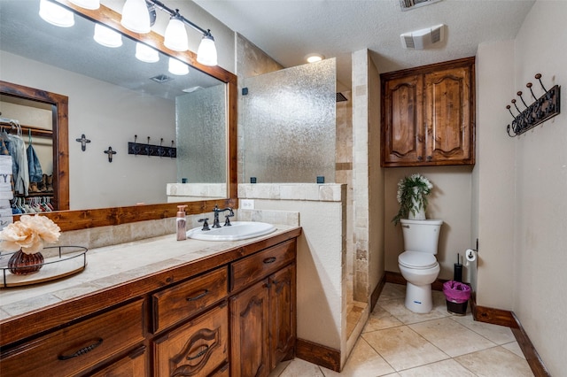 bathroom featuring tiled shower, toilet, a textured ceiling, vanity, and tile patterned flooring