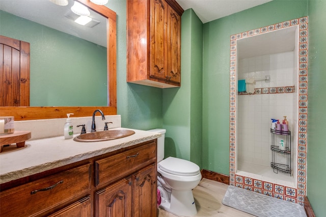 bathroom featuring hardwood / wood-style flooring, vanity, toilet, and a tile shower