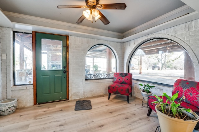 foyer entrance featuring crown molding, brick wall, wood-type flooring, and ceiling fan