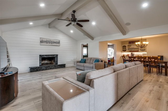 living room with ceiling fan with notable chandelier, a premium fireplace, light hardwood / wood-style floors, and lofted ceiling with beams