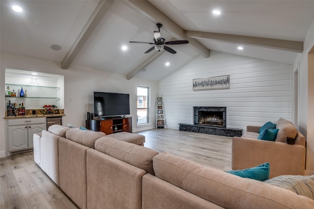 living room featuring vaulted ceiling with beams, indoor bar, a stone fireplace, and light wood-type flooring