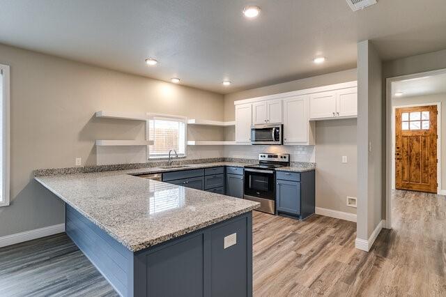 kitchen featuring appliances with stainless steel finishes, light stone countertops, white cabinets, kitchen peninsula, and light wood-type flooring