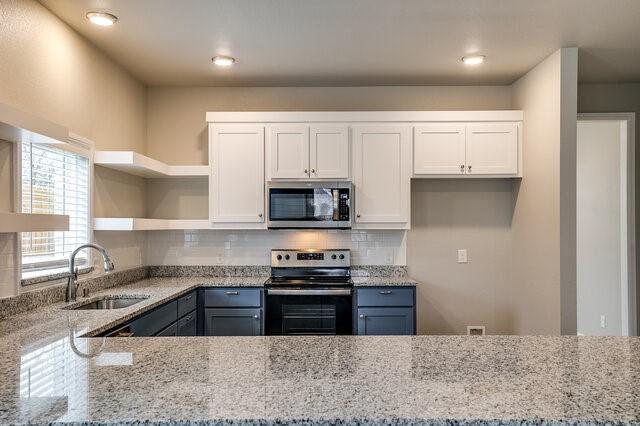 kitchen with sink, light stone counters, tasteful backsplash, appliances with stainless steel finishes, and white cabinets