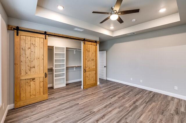 unfurnished bedroom featuring a closet, hardwood / wood-style flooring, a raised ceiling, and a barn door