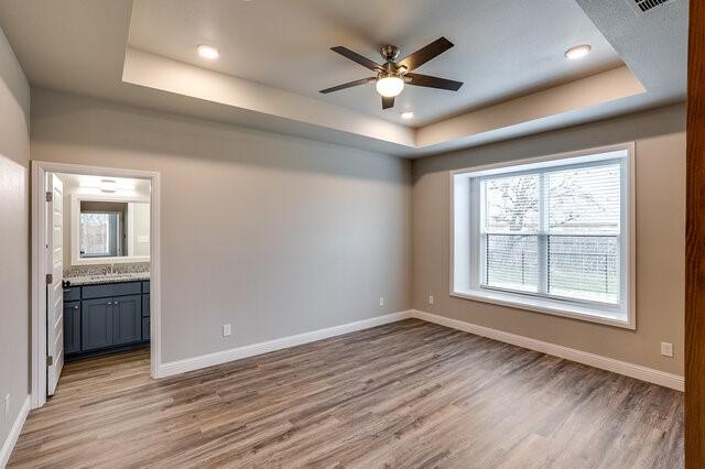 spare room with ceiling fan, a tray ceiling, and light hardwood / wood-style flooring