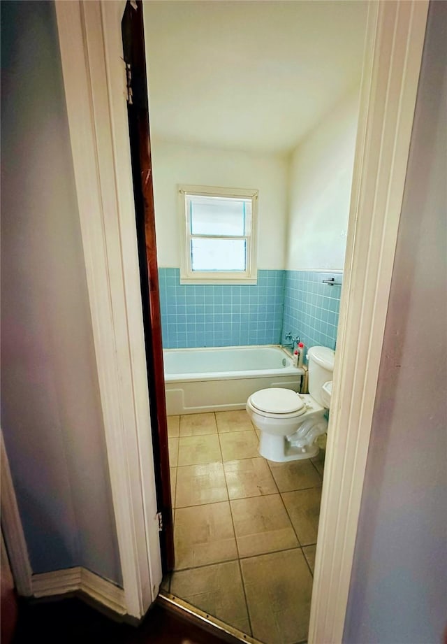 bathroom with tile patterned flooring, a washtub, toilet, tile walls, and wainscoting