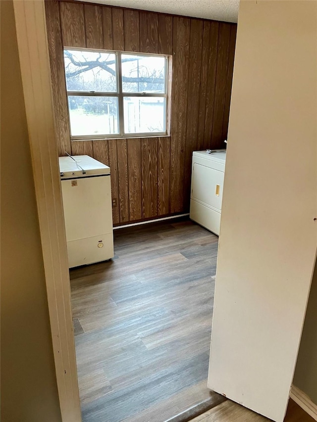 clothes washing area with wood walls, a textured ceiling, wood finished floors, washer / dryer, and laundry area