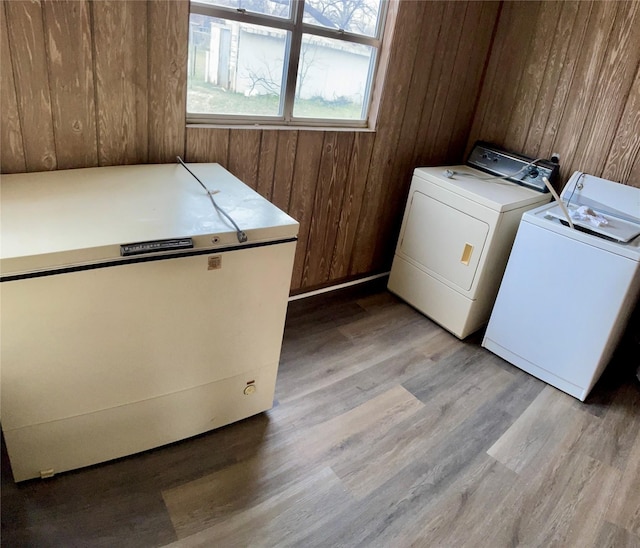 laundry area with laundry area, wood walls, light wood-type flooring, and washer and dryer