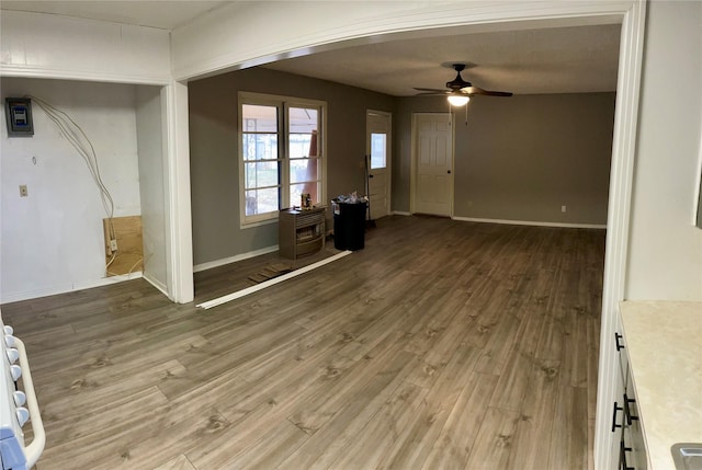 unfurnished living room with ceiling fan, light wood-type flooring, and baseboards