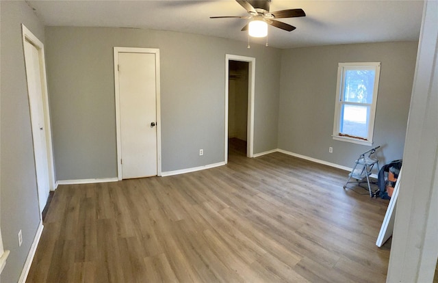 unfurnished bedroom with a ceiling fan, a spacious closet, baseboards, and wood finished floors