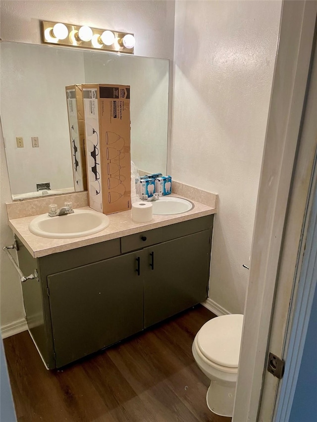 bathroom with double vanity, toilet, a sink, wood finished floors, and baseboards