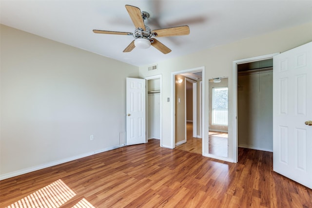 unfurnished bedroom featuring ceiling fan, dark hardwood / wood-style flooring, and two closets