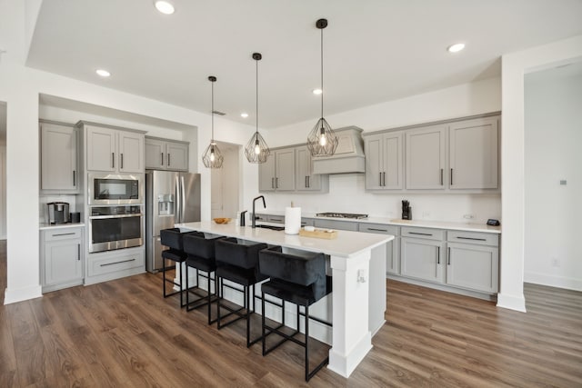 kitchen with gray cabinets, premium range hood, appliances with stainless steel finishes, and a kitchen breakfast bar