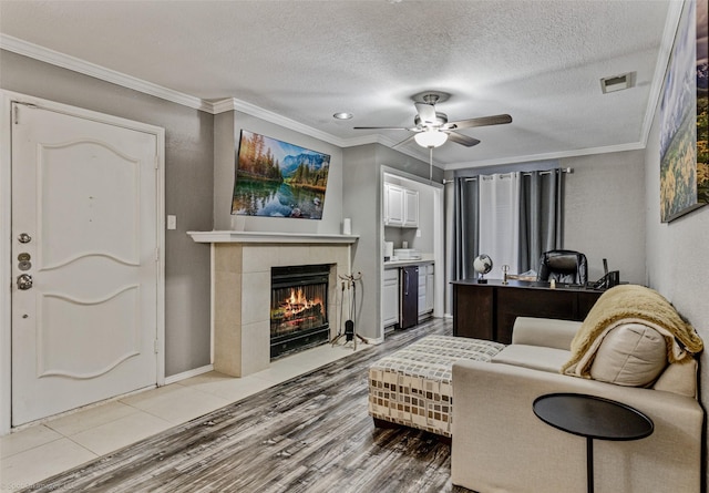 living area with visible vents, ornamental molding, a ceiling fan, light wood-style floors, and a tile fireplace
