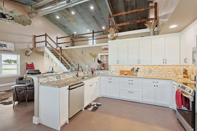 kitchen with white cabinetry, appliances with stainless steel finishes, kitchen peninsula, a towering ceiling, and light stone countertops