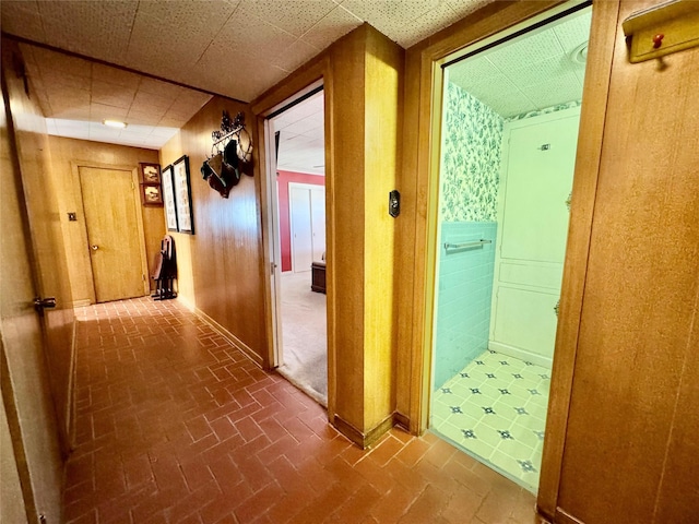 hallway featuring wooden walls and a drop ceiling