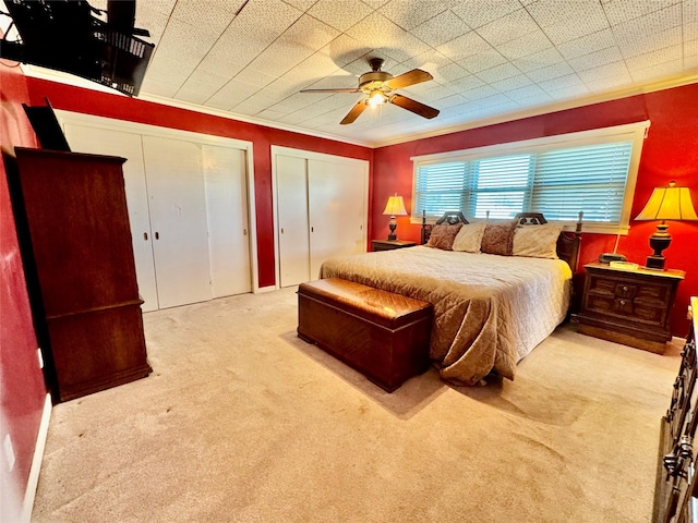 bedroom with multiple closets, ornamental molding, light colored carpet, and ceiling fan