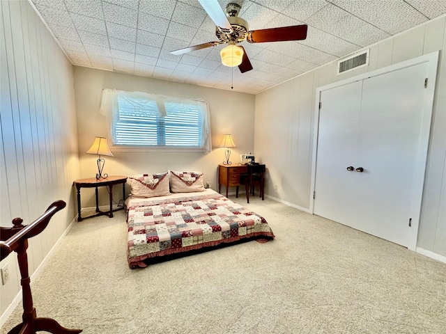 carpeted bedroom with ceiling fan and wooden walls