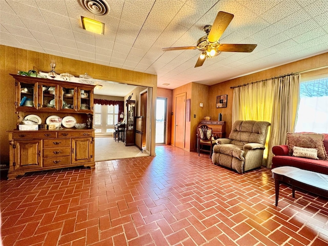 living room featuring a wealth of natural light, ceiling fan, and wood walls