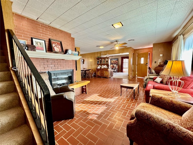 living room with ceiling fan, a fireplace, and wood walls