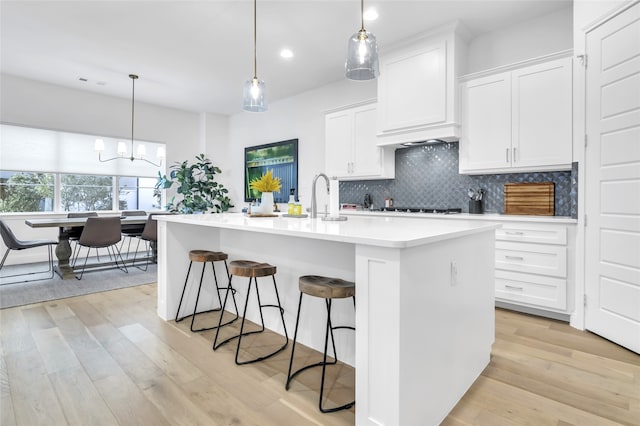 kitchen featuring pendant lighting, tasteful backsplash, white cabinets, a center island with sink, and light hardwood / wood-style flooring