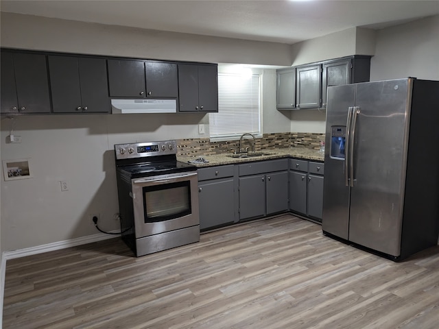 kitchen with gray cabinets, appliances with stainless steel finishes, sink, light stone countertops, and light hardwood / wood-style flooring