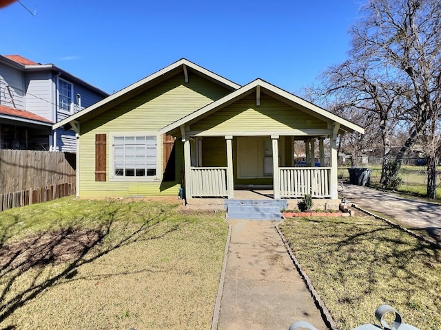 bungalow-style house with covered porch, fence, and a front lawn