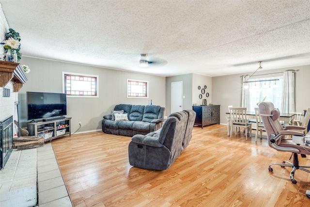 living room featuring a textured ceiling, a fireplace, a healthy amount of sunlight, and light wood-type flooring