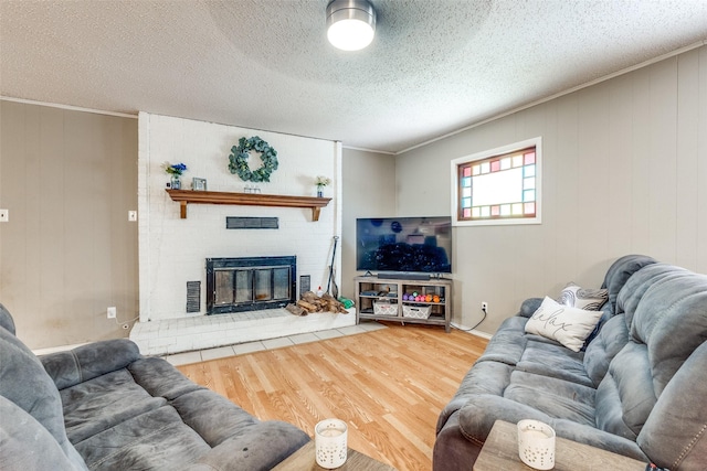 living room with crown molding, wood-type flooring, a brick fireplace, and a textured ceiling