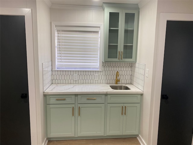 kitchen featuring tasteful backsplash, green cabinetry, glass insert cabinets, light stone countertops, and a sink