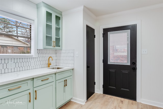 kitchen featuring decorative backsplash, ornamental molding, a sink, light wood-type flooring, and green cabinetry