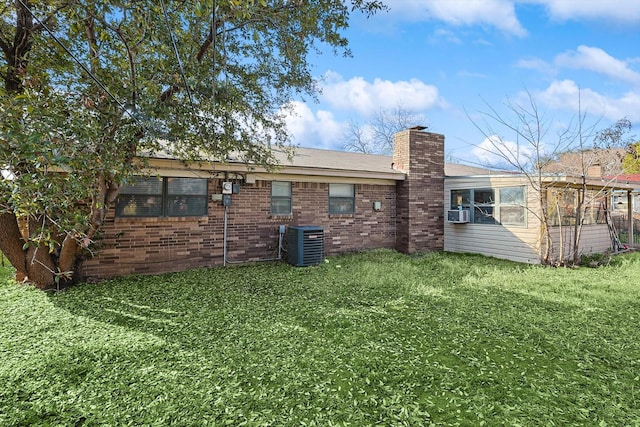 rear view of property with cooling unit, central air condition unit, and a lawn