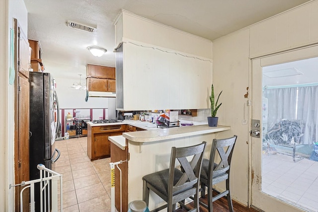 kitchen with stainless steel appliances, a breakfast bar area, light tile patterned floors, and kitchen peninsula