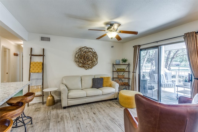 living room with ceiling fan, light hardwood / wood-style flooring, and a textured ceiling