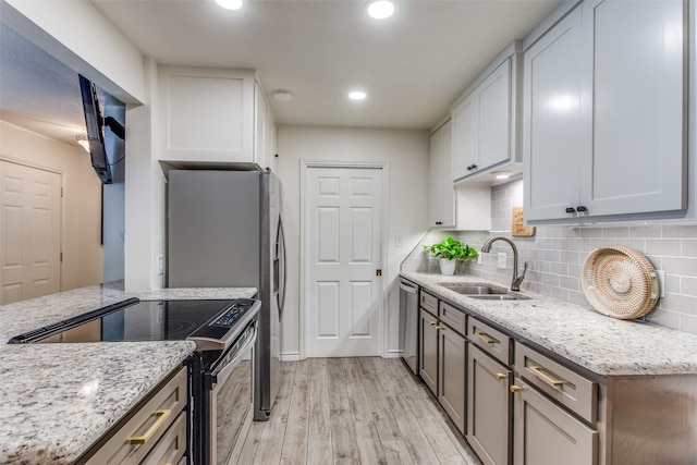 kitchen with stainless steel appliances, sink, light stone counters, and light hardwood / wood-style flooring