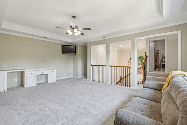 living room with built in desk, ornamental molding, light colored carpet, ceiling fan, and a raised ceiling