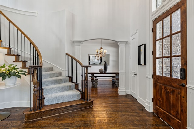 entryway with dark hardwood / wood-style floors, a chandelier, decorative columns, and a high ceiling