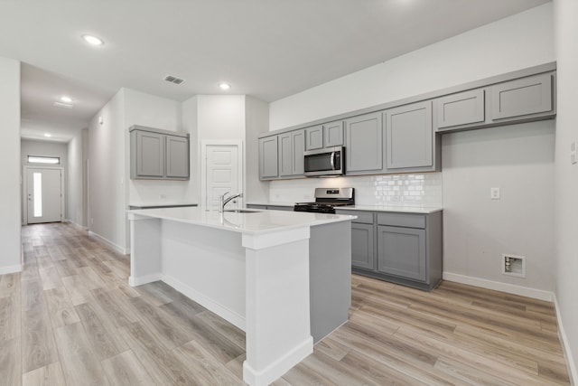 kitchen featuring tasteful backsplash, sink, gray cabinetry, a kitchen island with sink, and stainless steel appliances