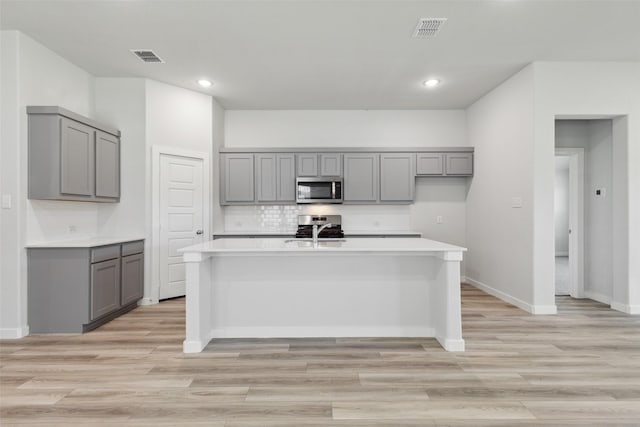 kitchen featuring a kitchen island with sink, gray cabinets, light hardwood / wood-style floors, and appliances with stainless steel finishes