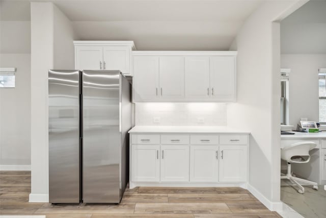 kitchen with stainless steel fridge, light wood-type flooring, decorative backsplash, and white cabinets